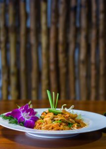 Aromatic Thai Pad Thai with noodles, shrimp, and elegant orchid garnishing on a white plate.