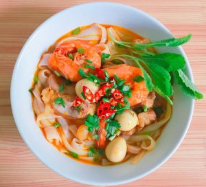 A vibrant bowl of Vietnamese noodle soup with shrimp, herbs, and quail eggs.