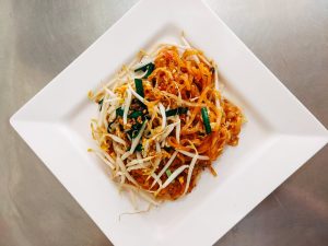Top view of a savory Pad Thai dish garnished with fresh vegetables on a white plate.