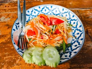 Vibrant close-up of Thai papaya salad with fresh vegetables on a traditional plate.