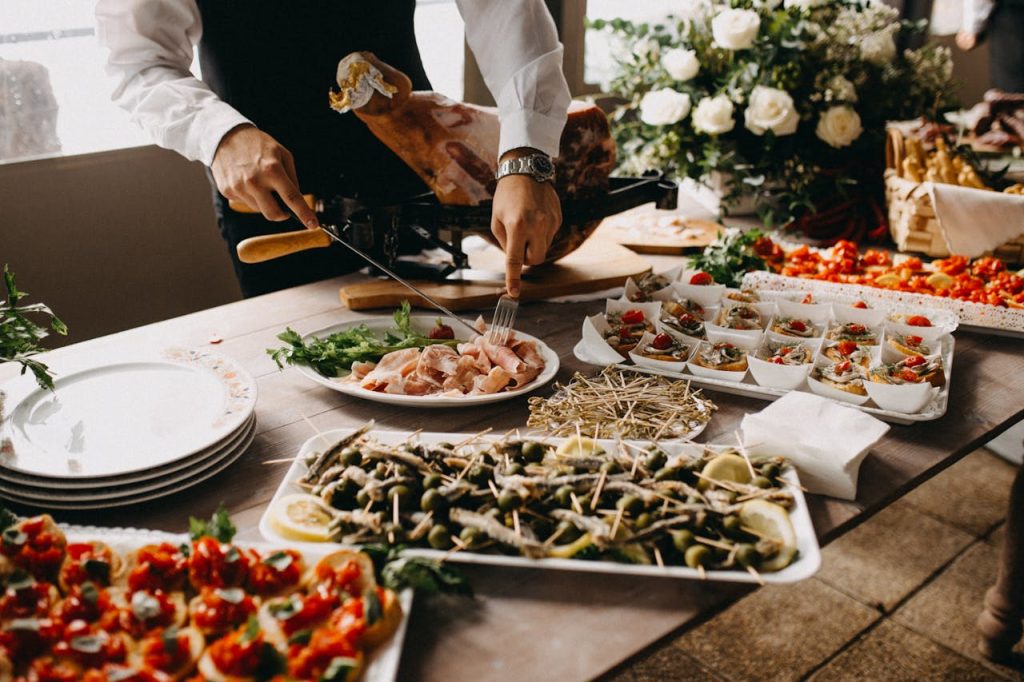 standing-person-using-fork-and-knife-on-preparing-food-2814828 A chef slices meat in a beautifully arranged catering setup with diverse appetizing dishes.